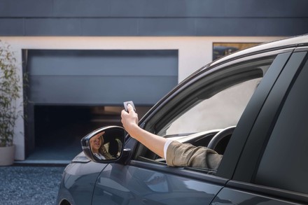  Kobieta siedząca w samochodzie otwiera automatyczną bramę garażową za pomocą pilota.